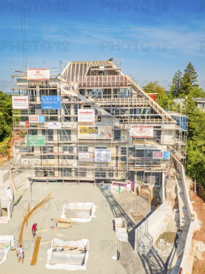 Construction site of a large building with several floors, surrounded by trees and scaffolding,