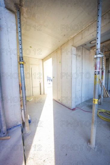 A sunlit corridor in an unfinished building with concrete walls and metal supports, carpentry