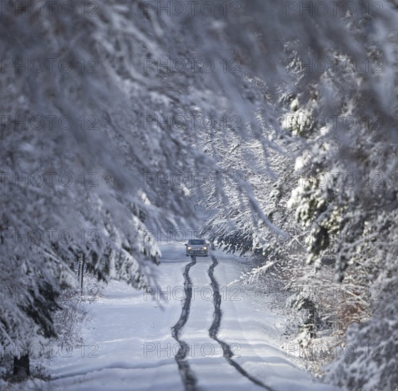 Car driving in lane across heavily snow-covered road with heavy amounts of snow through a winter