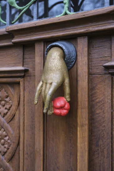 A cast iron door knocker on a wooden, artfully decorated front door in the shape of a hand holding
