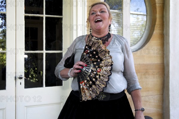 Laughing woman with decorative fan standing in front of an elegant entrance, Houmas House,
