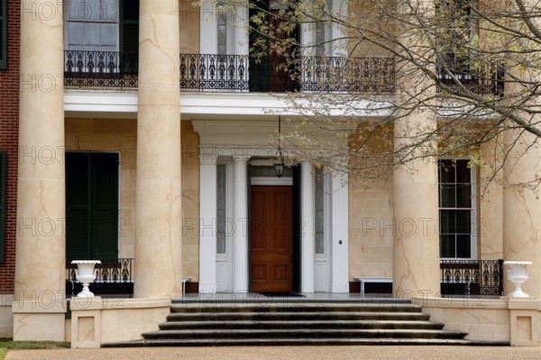 Entrance of an elegant house with large pillars and wooden door, surrounded by trees, Natchez,