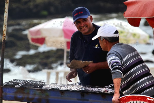 Two men talking at a food stall on the shore with a view of the sea, Oulidia, Doukkala-Abda,