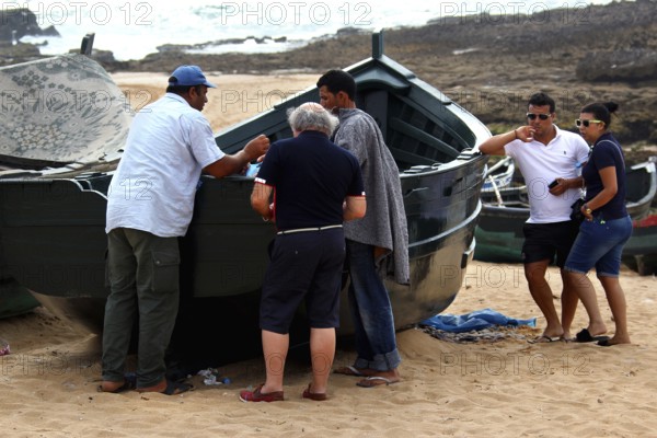Group of people gather around a fishing boat on the beach in Oulidia, Oulidia, Doukkala-Abda,