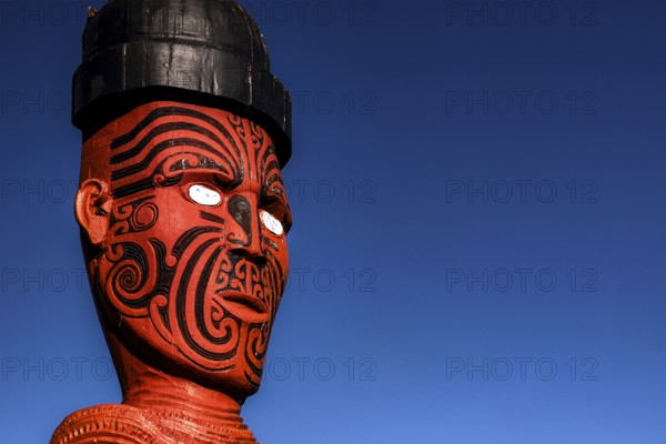 Large carved Maori figure painted red against deep blue sky in Whakarewarewa village, Rotorua,