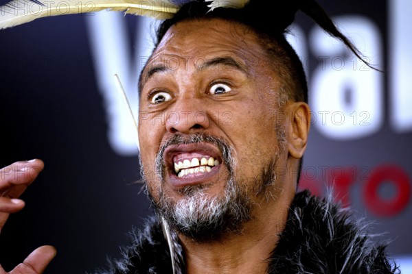 Maori man with aggressive facial expressions and feather headdress at a performance, Rotorua, Bay