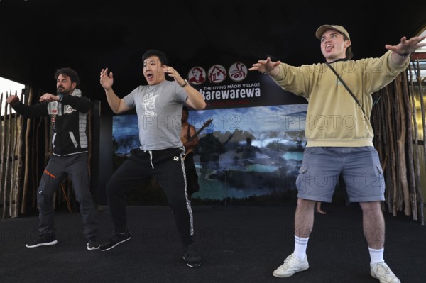 Three tourists taking part in a Haka performance and having fun on stage, Rotorua, Bay of Plenty,