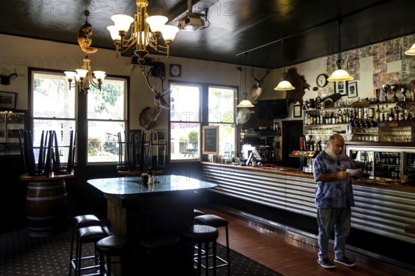 Atmospheric hotel bar with vintage decor and a man at the bar, Whangamomona, New Zealand