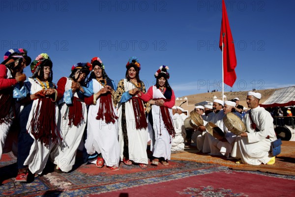Women perform traditional Berber dance with an ensemble of musicians in the background under a blue