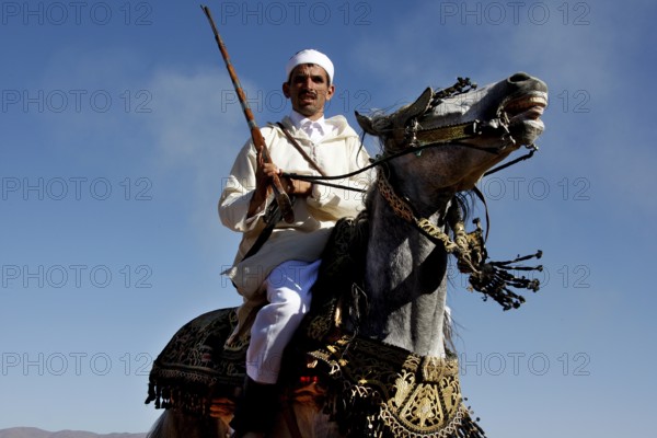 A man in traditional traditional costume rides a magnificently decorated horse under a blue sky, El