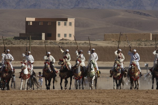 Riders in formation on a wide terrain with mountain scenery during Fantasia, El Kelâa m'Gouna,