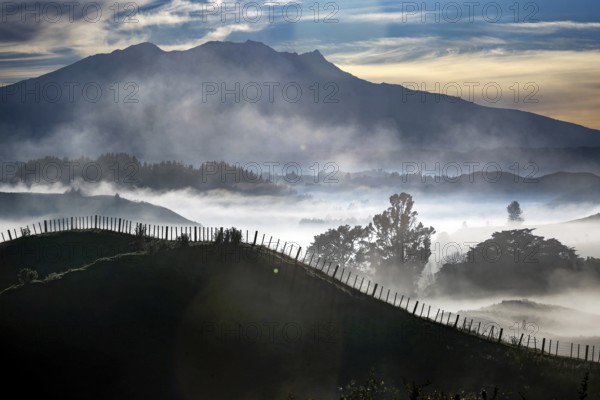 Morning fog envelops rolling hills and shimmers between fences and mountains in the distant