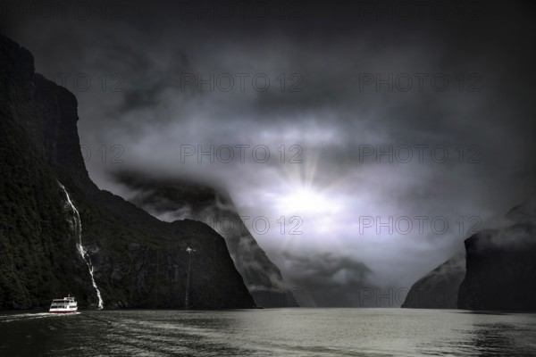 Fjord landscape with a cruise ship, sun rays breaking through the cloud cover, Milford Sound, New