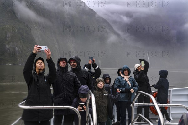 Group of passengers take pictures of the misty landscape from a cruise ship, Milford Sound, New