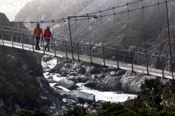 Hikers crossing a suspension bridge in a misty mountain landscape, Mt Cook, Hocker Valley Track,