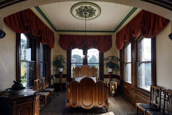 Comfortable bedroom with fine furnishings, large windows and red curtains, Larnach Castle, Otago