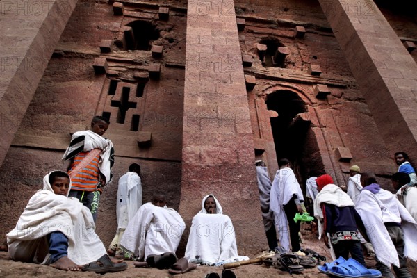 Pilgrims wearing white cloaks gather solemnly in front of the Bete Medhane Alem rock church at