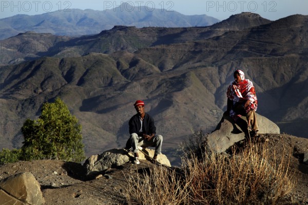Two people sit in front of the impressive mountain scenery of the Lasta Mountains, Lalibela,