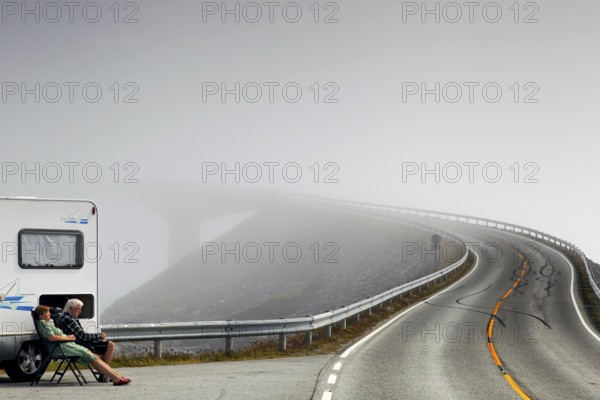 Camper sitting on the side of the road on the foggy Atlantic road with steeply rising asphalt,