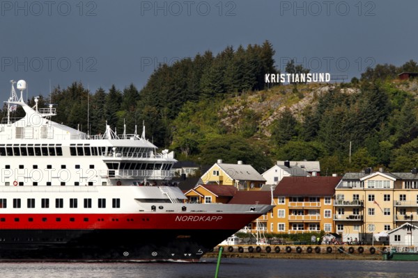 Hurtigruten ship off the coast of Kristiansund with colorful houses and forest, Kristiansund, Møre