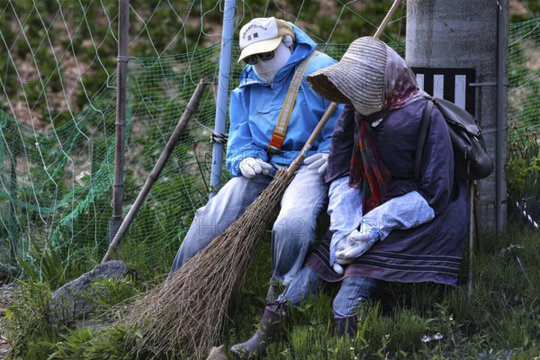 Two fabric figures sitting in the garden holding brooms