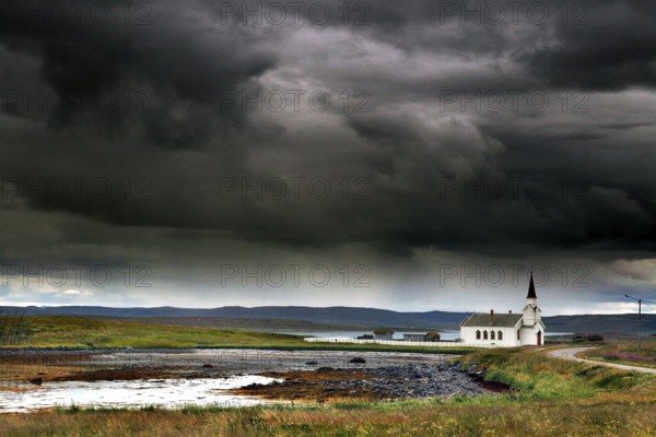 Small church in Nesseby under thick, dramatic clouds in the sky, Nesseby, Finnmark, Norway