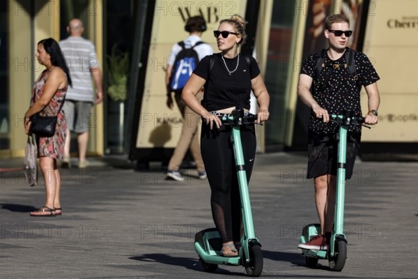 Two people ride scooters on a road in Tallinn when the sun is shining, Tallinn, South Alinn,