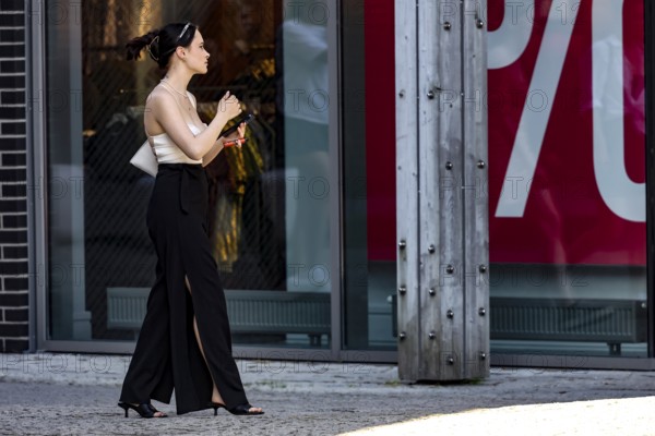 Woman walks by a shop while holding a cellphone and strolling through the neighborhood, Tallinn,
