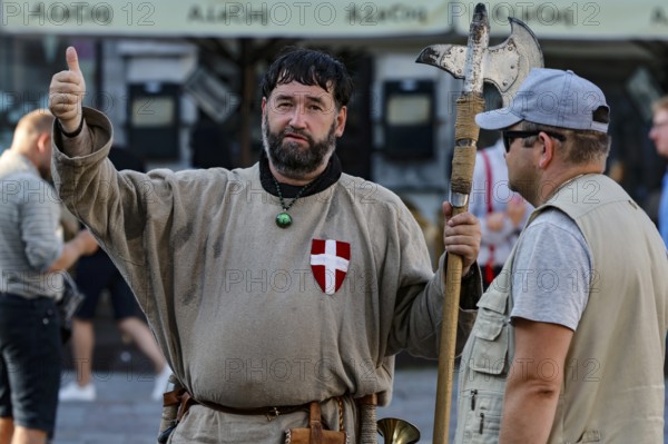 Two men, one in medieval traditional costume with an axe, on a busy square in Tallinn, Tallinn,