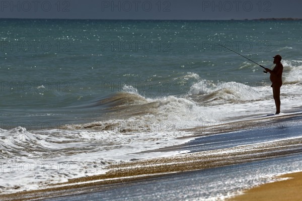 Angler standing on the beach fishing in the waves of Cable Beach, Broome, Broome, Western