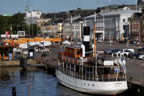 The market square in Helsinki with a boat and historic buildings along the busy harbor promenade,