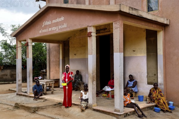 People sit and stand in front of a hospital building. The surrounding area seems quiet, Bouké,