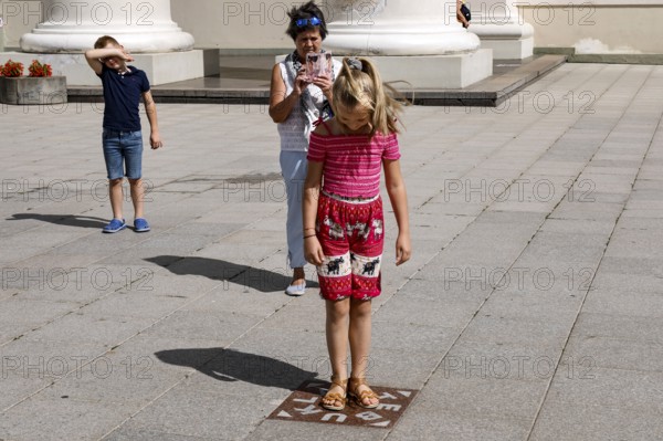 Child standing on miracle tile while tourists capture the moment, Vilnius, Vilnius County,