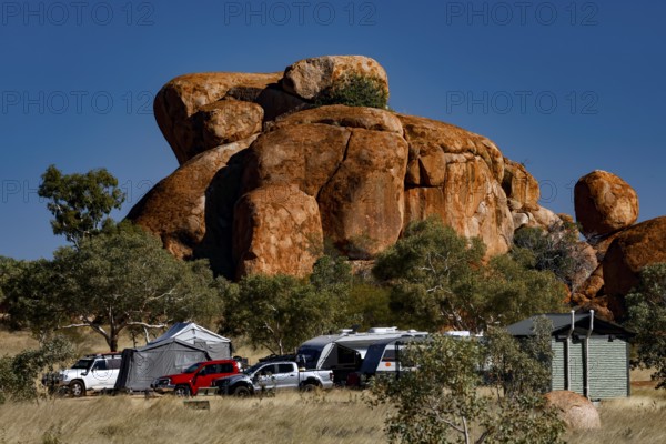 Campground surrounded by distinctive red rocks and vehicles under blue skies, Devil's Marbles,