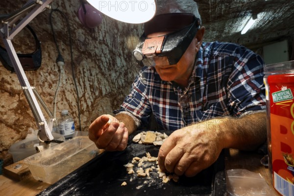 Miner examining opals at work light at Tom's Working Opal Mine, Coober Pedy, South Australia,