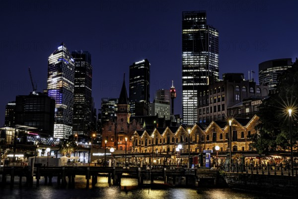 Night view of The Rocks in Sydney with illuminated former warehouses and modern skyscrapers,