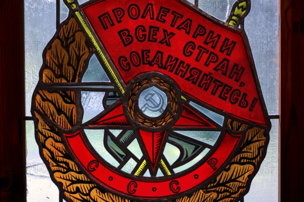Socialist coat of arms with red banners and symbols in a stained glass window in Grutas Park,
