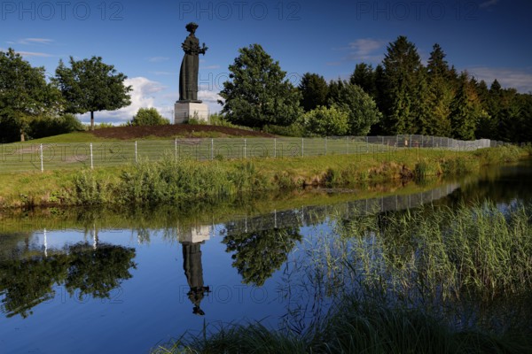Socialist statue in Grutas Park is reflected in a calm body of water surrounded by trees,