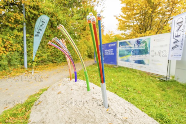 Colorful fiber optic cables sticking out of a pile of soil on a green area, fiberglass