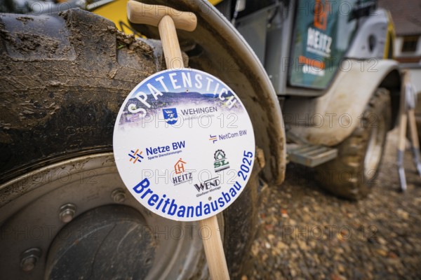 A sign announces broadband expansion, in the background a wheel loader on muddy ground, fiberglass