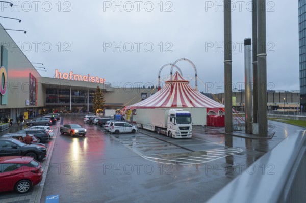 Shopping center parking lot in case of rain with illuminated circus tent at dusk, Böblingen,