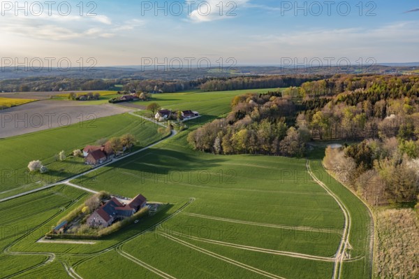 Green fields and forests with small farms under blue spring sky, oblique aerial view, Osnabrücker
