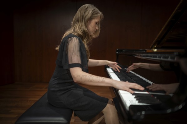 Young woman, pianist, side view playing on a Steinway & Sons grand piano in evening dress,