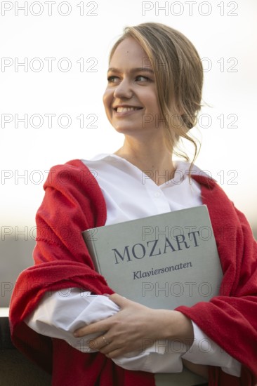 Smiling young woman, pianist, in white blouse and red cardigan, in the evening light, holding notes