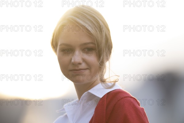 Serious looking young woman in white blouse and red cardigan, in backlight, Stuttgart,