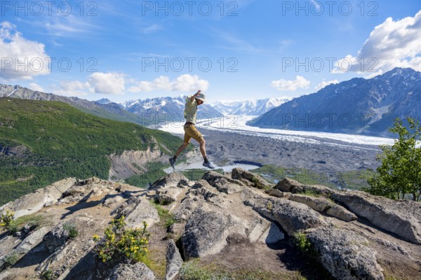 Young man jumping into the air, view of impressive mountain landscape with Matanuska glacier and
