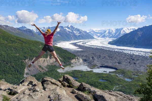 Young woman jumping into the air, view of impressive mountain landscape with Matanuska glacier and