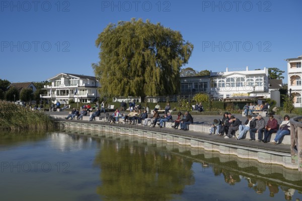 Tourists sunbathe on the promenade, Schmachter See, spa architecture buildings in the back, Binz,