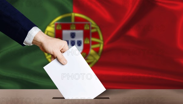 Hand placing a ballot in ballot box with the Portuguese flag in the background. Portugal