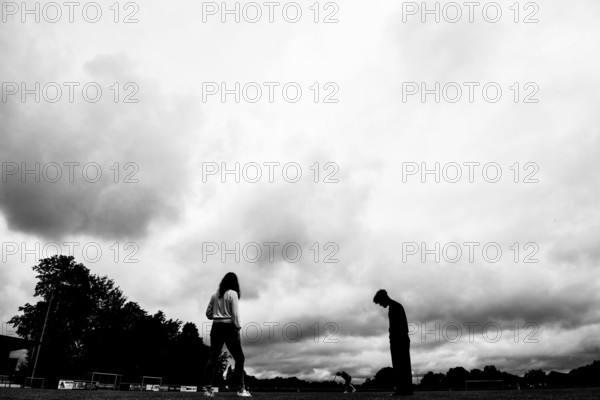 Two silhouettes of people under dramatically cloudy sky on a sports field, sports and fun Olympics